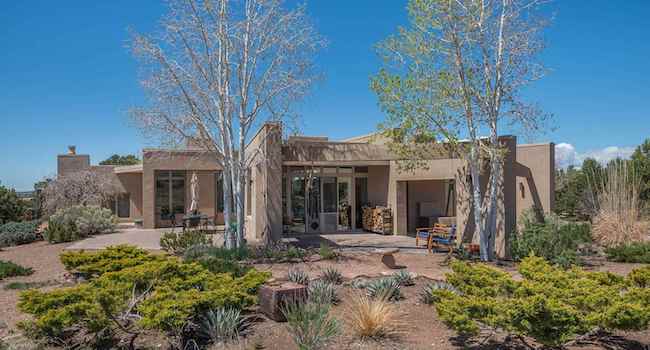 A home for sale in Santa Fe with an adobe exterior and front yard landscaped with two trees and an array of low shrubs