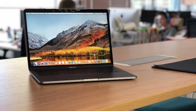 A laptop sitting on a desk with a home screen of mountains