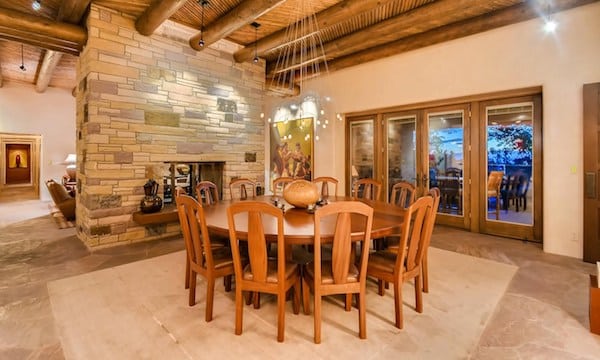 The dining room of a Santa Fe home with a round table placed in front of a stone double fireplace.
