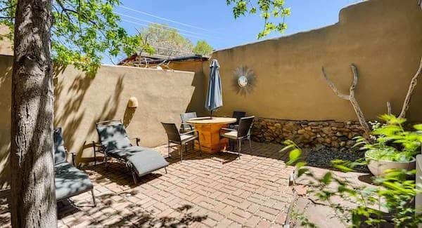 The backyard of a Santa Fe home with a high adobe wall and patio furniture