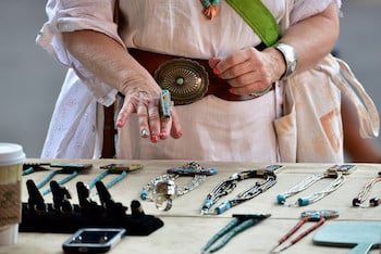 A display of silver and turquoise jewelry at the Santa Fe Indian Market in Santa Fe, New Mexico. A woman's hand models a ring.