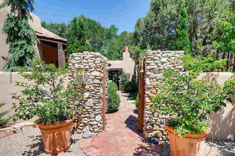 A home in Santa Fe with a courtyard entrance framed by a river-rock doorway flanked by two trees in terra cotta pots