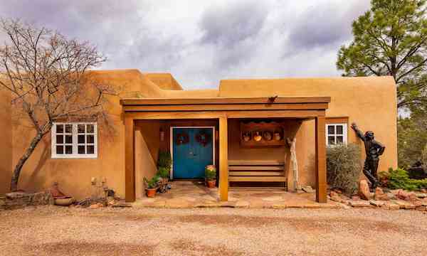 The exterior of a Santa Fe home designed in the Pueblo Revival style with adobe walls and a bright turquoise front door.