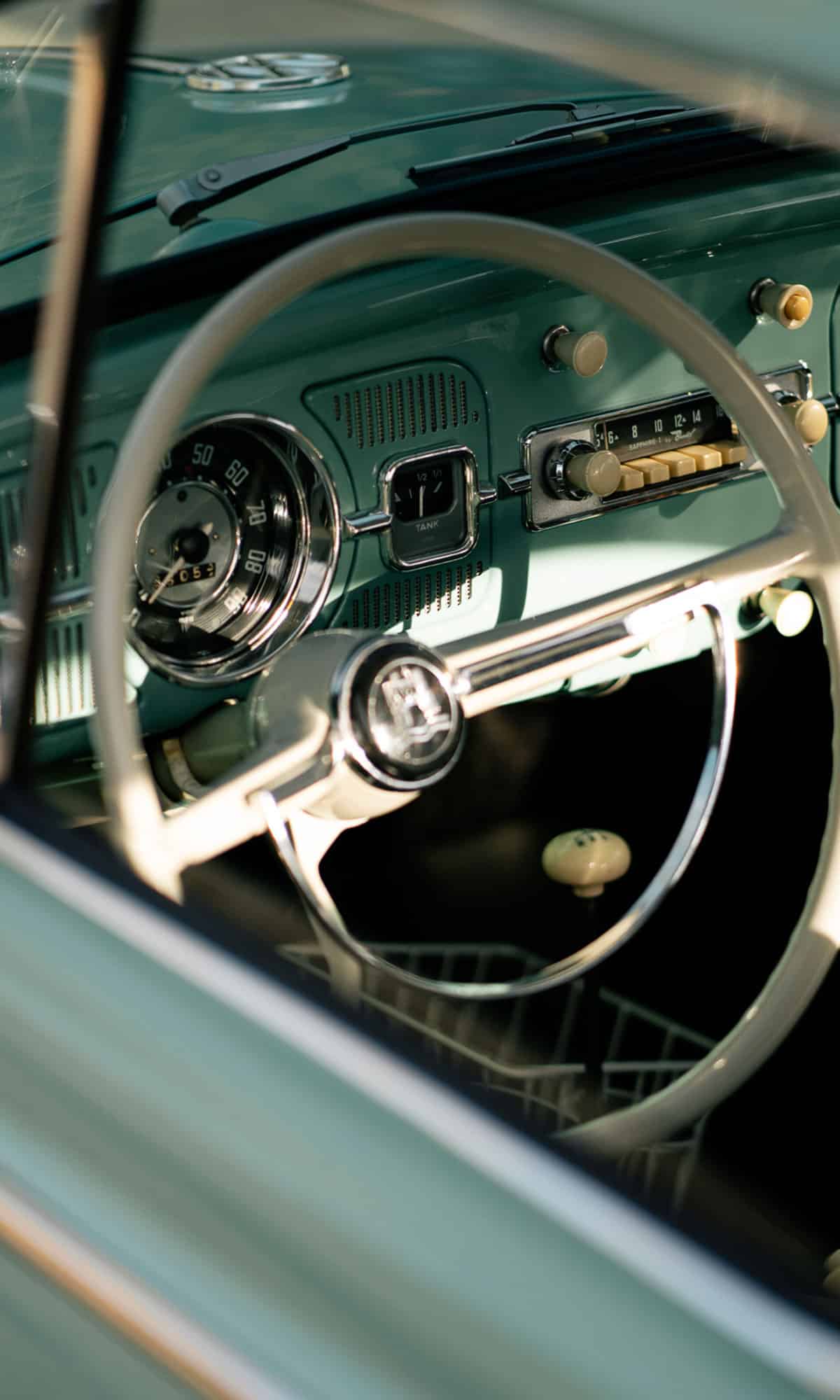 The wheel and dashboard of a well restored, turquoise Volkswagen Beetle from the 1960's.