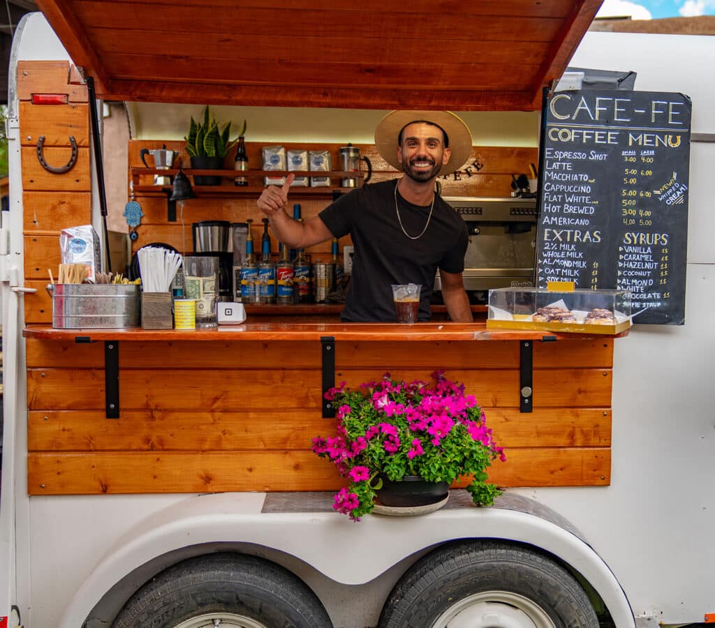 Friendly smiling man wearing a hat in coffee trailer with menu and flowers in Santa Fe, New Mexico.