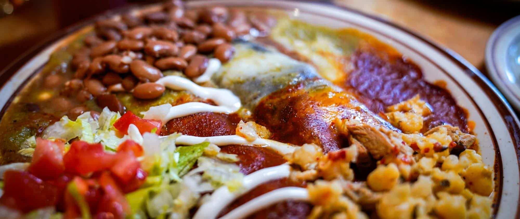A detail of a plate of New Mexican food featuring red and green chile, pinto beans, and posole.