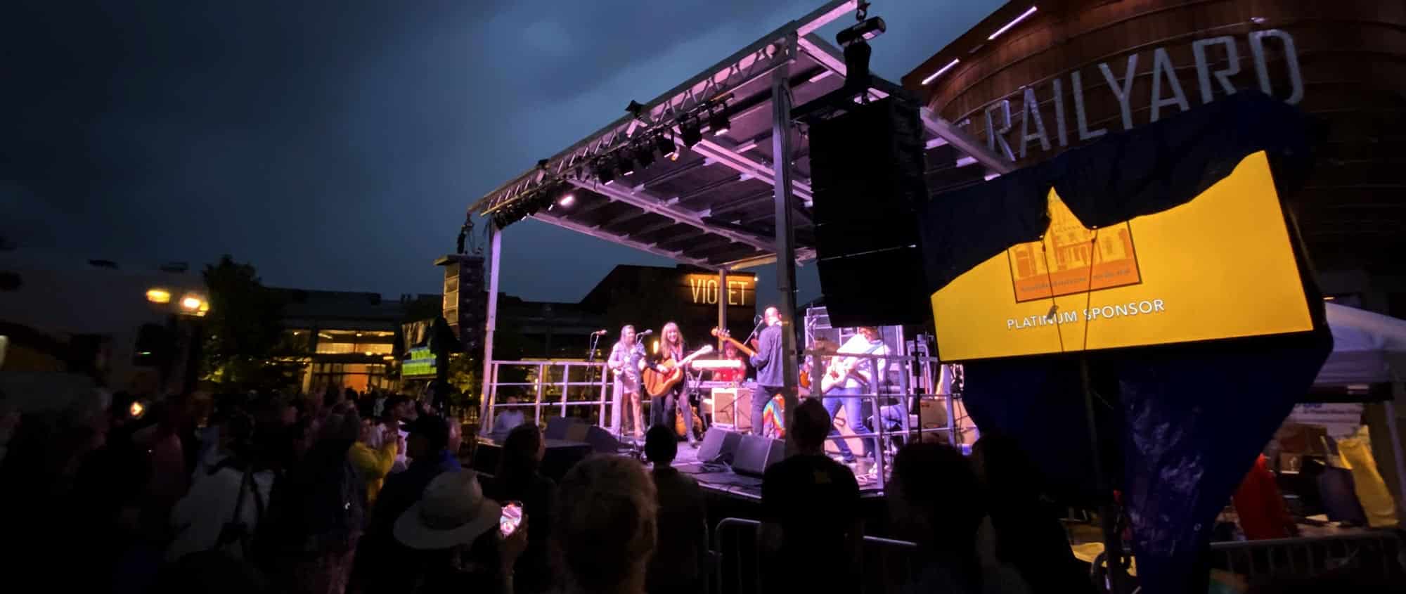 A lit stage with musicians in the Railyard.