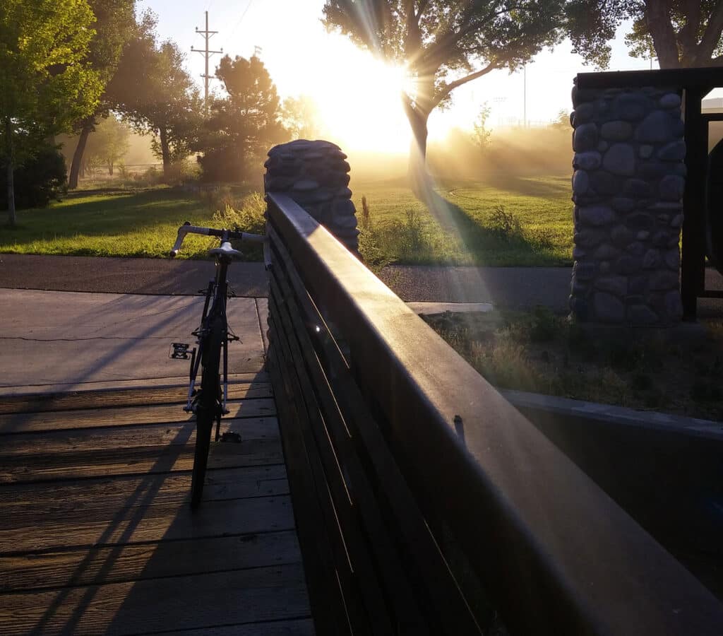 Bicycle leaned against iron and stone bridge, looking out in to a green misty park and setting sun.