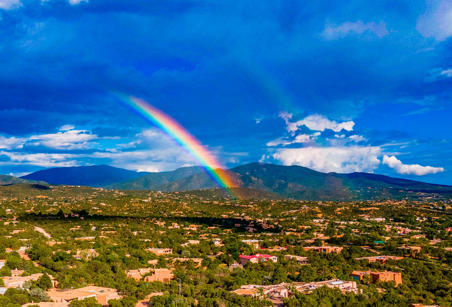 A landscape looking toward the Sangre de Christo Mountains with a bright rainbow over Santa Fe, New Mexico.