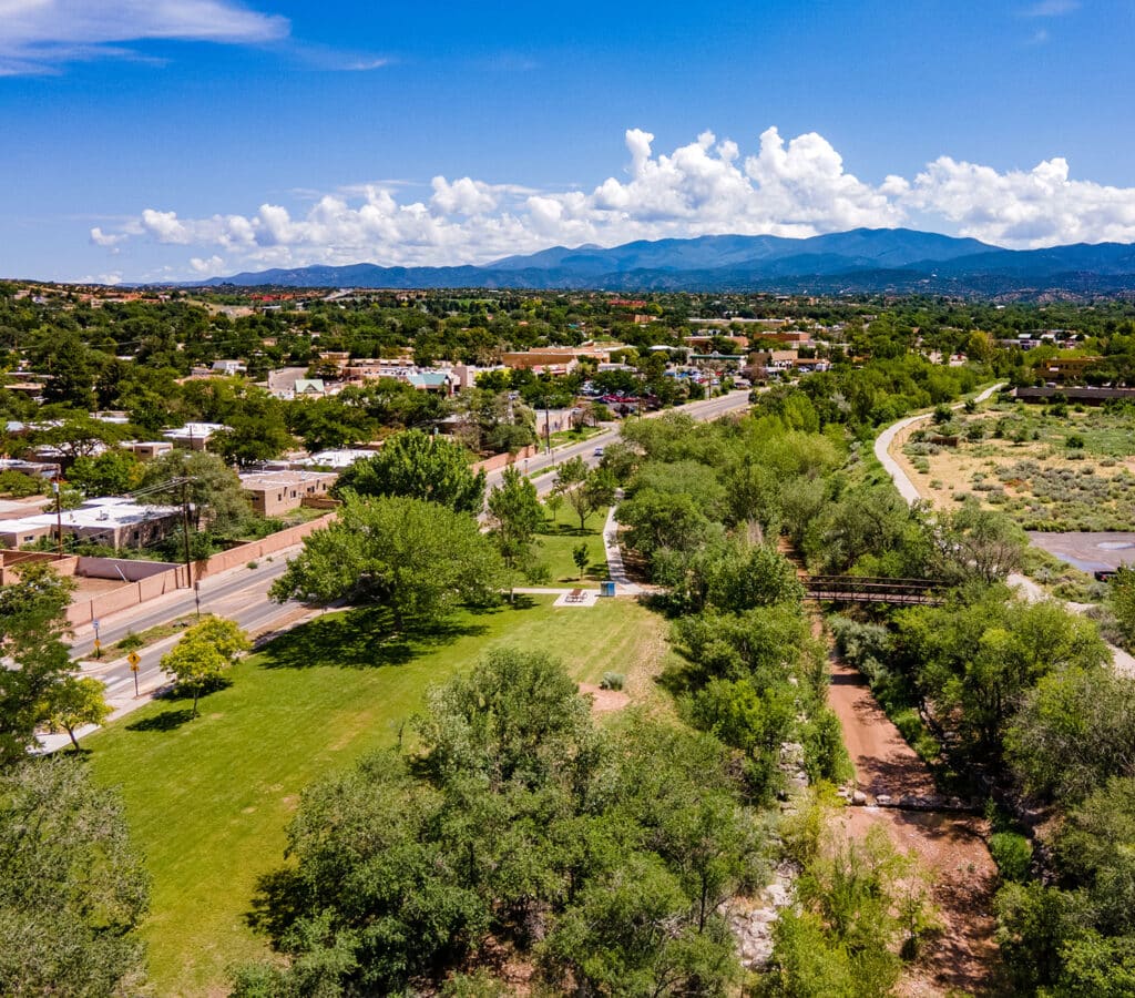 Aerial view of Santa Fe River, a park, and foot bridge over looking town and mountains.